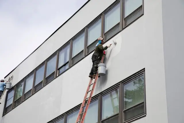 Painter in safety gear rolling paint on a commercial building exterior