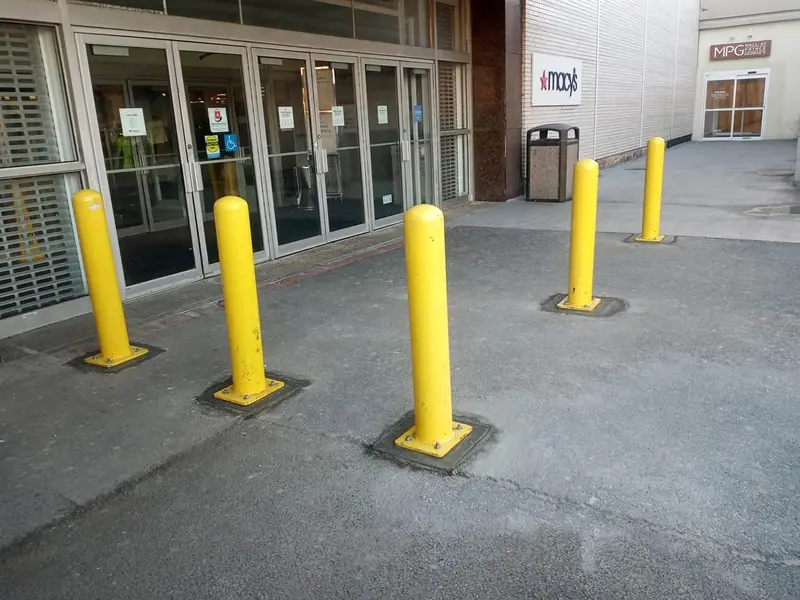 Five yellow safety bollards installed in front of a Macy’s store entrance