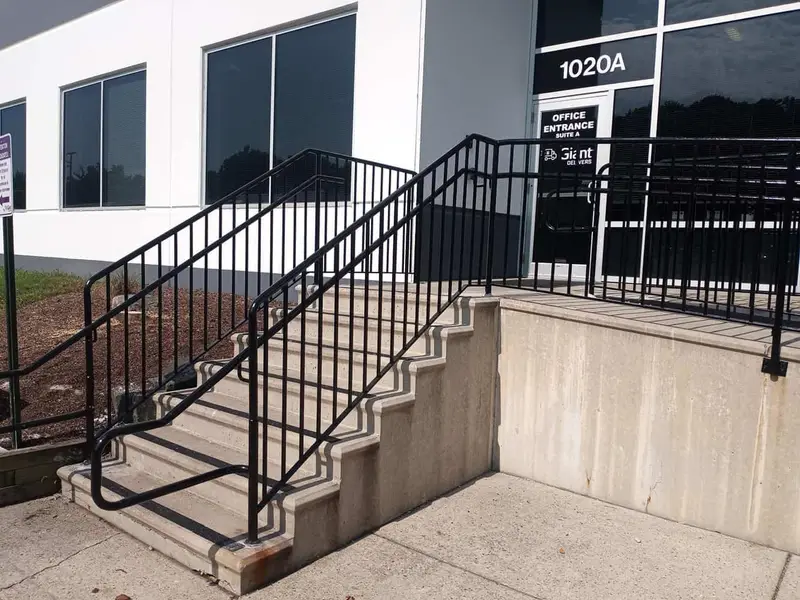 New concrete steps and black metal railings at a glass office entrance labeled 1020A