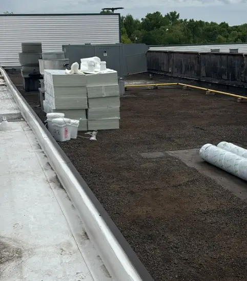 Commercial roof tear-off in progress with stacked polyiso insulation boards and rolled membrane staged on the deck