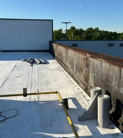 New white TPO membrane along a parapet wall with membrane rolls staged for installation