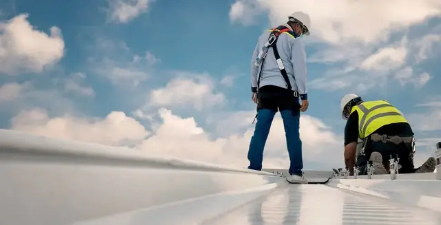 Two roofers in safety gear repairing a commercial roof