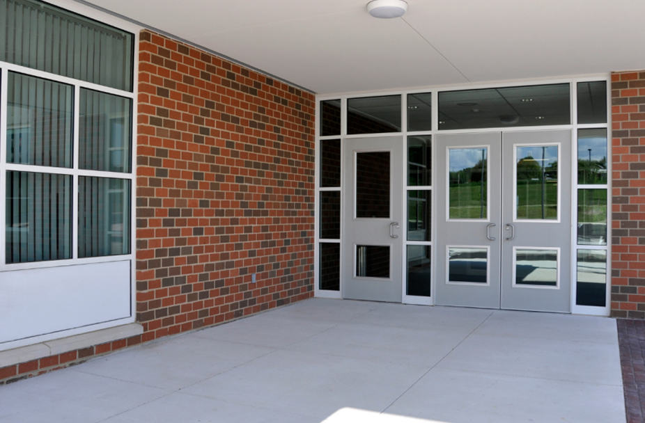 Building entrance with glass double doors, large windows, and red brick walls under a white overhang; ideal for commercial renovation and construction services.