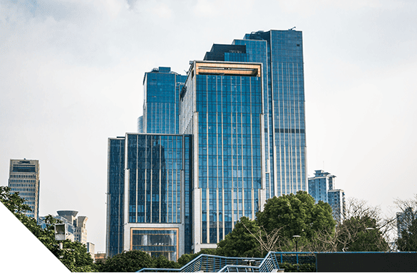 Modern glass skyscraper under cloudy sky with smaller buildings and trees in the foreground, showcasing elegant exterior renovation and contemporary architectural design.