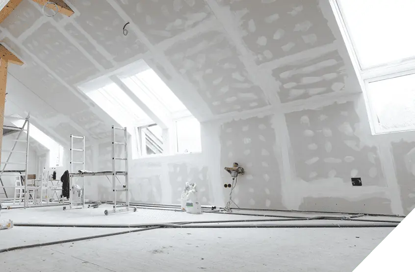 Unfinished attic space with installed drywall and skylights, showcasing renovation potential; ladders and construction materials on the floor for interior remodel projects.