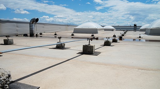 Flat rooftop with dome-shaped skylights, ventilation pipes, and concrete blocks under a partly cloudy sky; ideal for expert roofing renovation and maintenance services.