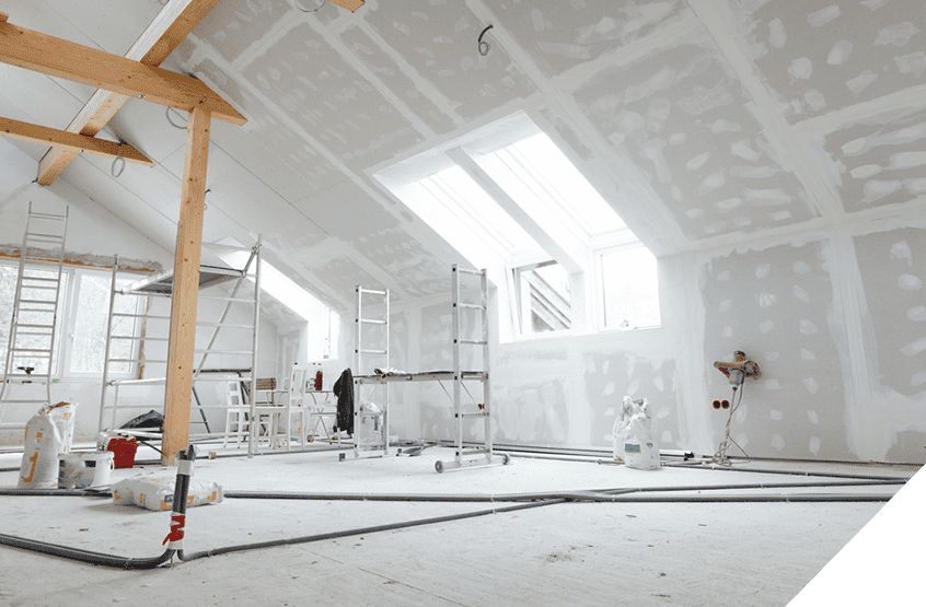 Room renovation in progress with ladders, scaffolding, and incomplete drywall; skylights provide natural light over scattered construction materials.