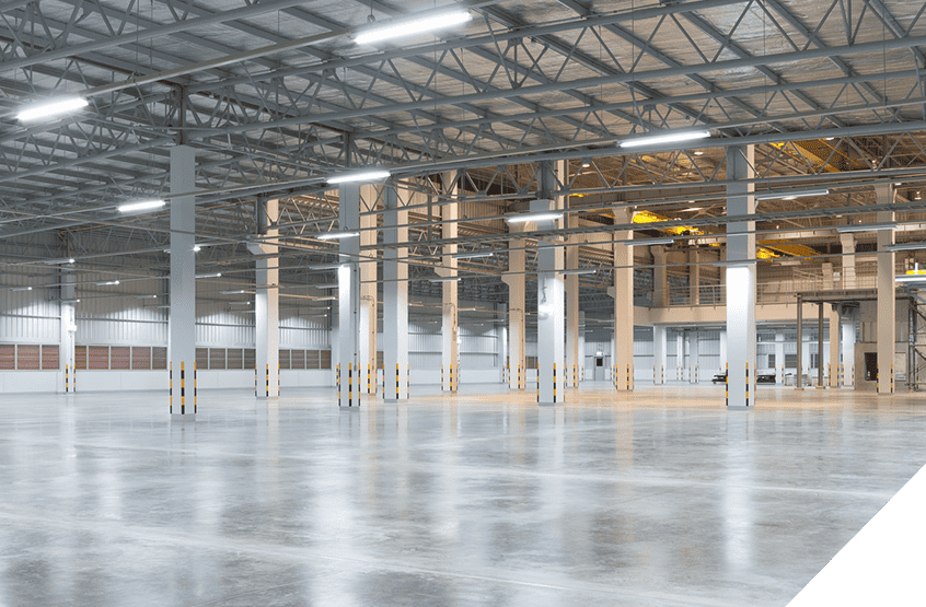 Industrial warehouse renovation with high ceilings, exposed beams, polished commercial flooring, and overhead lighting.