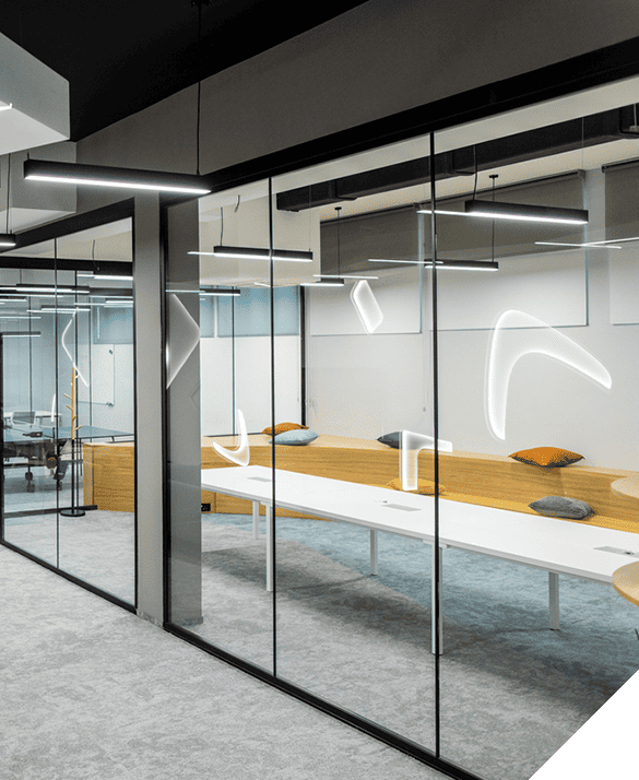 Image of a modern office space with sleek glass walls, promoting an open atmosphere, accompanied by a long white table ideal for collaborative meetings and curved wooden seating for comfort. Contemporary ceiling lights enhance the elegant design. Commercial glass repair services available for maintaining pristine condition.