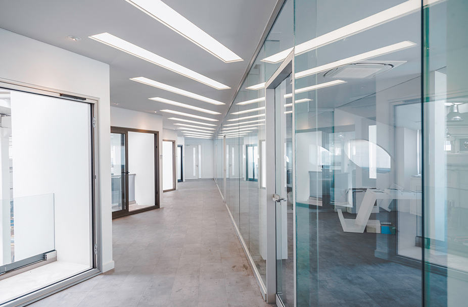 Modern office corridor with glass walls showcasing bright, minimalist interior design. Features doors seamlessly leading to adjacent rooms, emphasizing expert interior remodeling. Exterior and interior renovation services displayed.