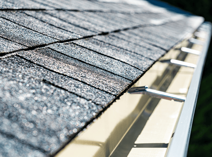 Close-up view of a shingled roof with light-colored gutters, showcasing seamless integration with expert siding services for exterior renovation.