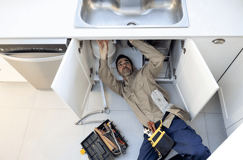 Image of a plumber repairing kitchen sink plumbing, tools scattered around, showcasing expert interior renovation services.