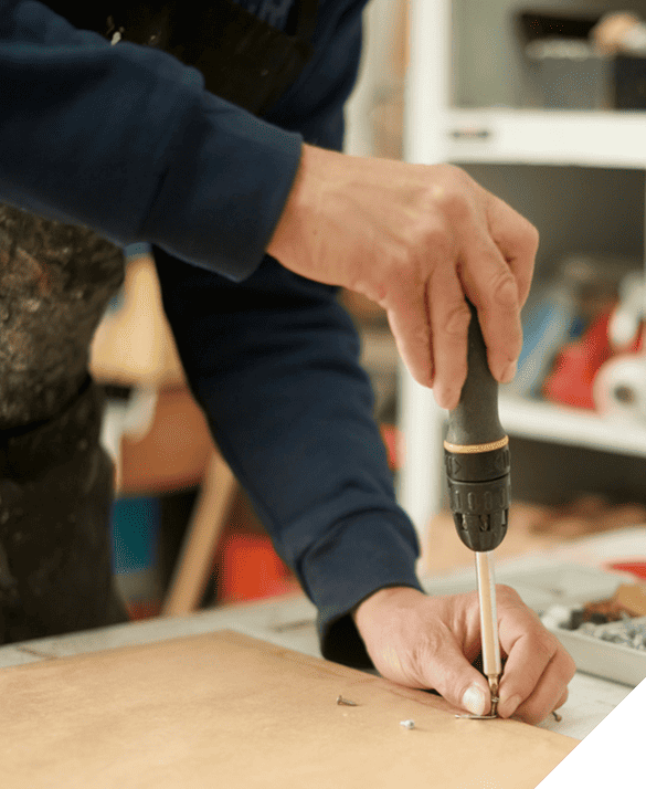 A skilled handyman using an electric drill to screw into a wooden board in a workshop, showcasing precision in renovation tasks.