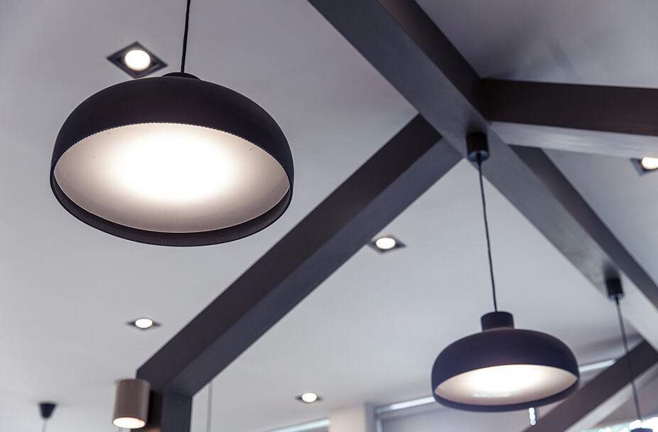 Modern interior remodeling with two black pendant lights hanging from a ceiling with exposed beams, complemented by recessed lighting for enhanced ambiance.