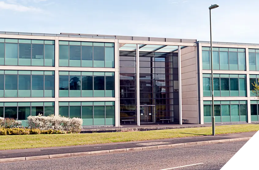 Modern three-story office building with green-tinted windows, central glass entrance, streetlamp, and grass verge. Exterior renovation and construction services.