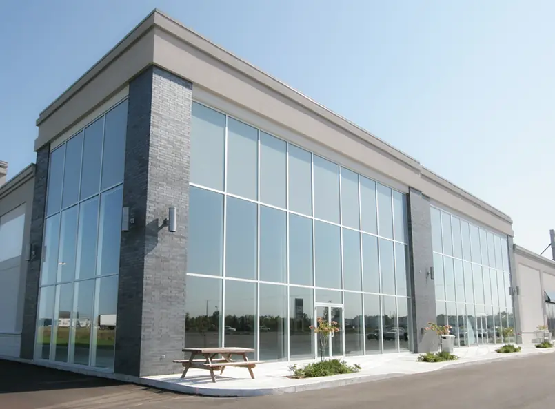 Modern commercial building with large windows and gray brick facade, featuring outdoor picnic bench and plants under blue sky; highlights expert window installation.