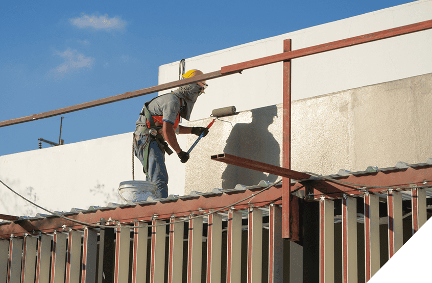 Construction worker in safety gear painting interior walls with roller brush on metal scaffolding, showcasing professional renovation services.