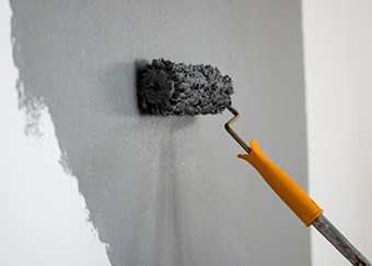 Gray paint applied to white wall with orange-handled roller; ideal for exterior and interior renovation services.