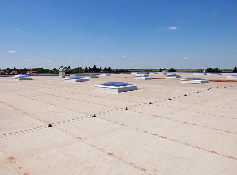 Flat rooftop with multiple skylights under clear blue sky, showcasing expert roofing renovation and construction services.