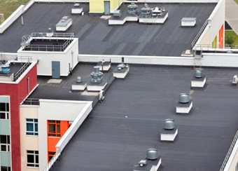 Aerial view of a flat-roofed building with ventilation units, skylights, window installations, and a vibrant facade in red, yellow, and white – ideal for exterior renovation inspiration.