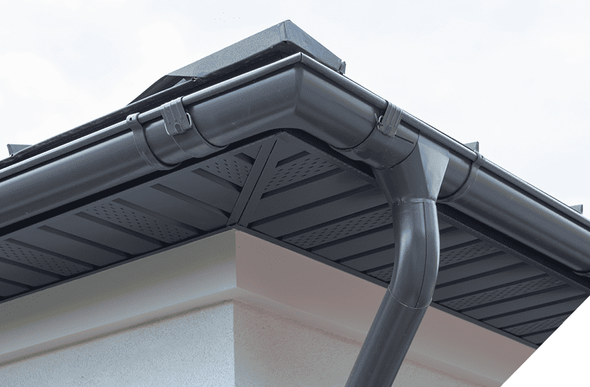 Close-up of modern house roof corner with black gutters, soffit, and downspout; highlights sleek design and expert siding services under cloudy sky.