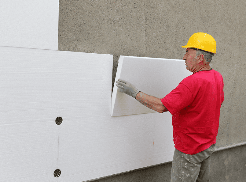 Construction worker installing white insulation panels on wall, demonstrating expertise in exterior renovation and remodeling services.