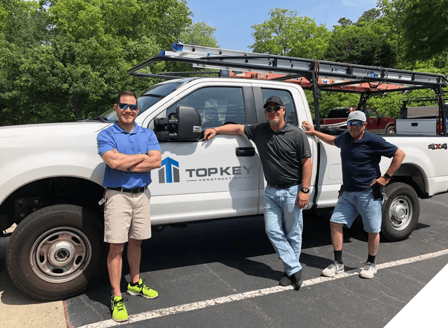 Three construction workers beside a white truck with ladders, set against a sunny outdoor backdrop with trees, illustrating dedication to top-tier renovation and construction services.