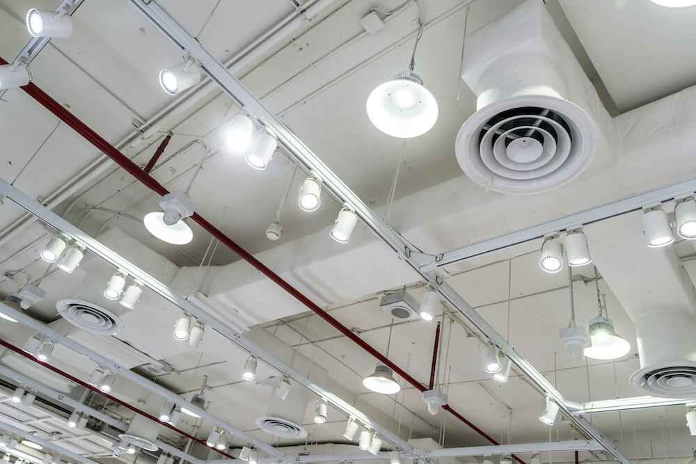 Ceiling view of modern commercial space featuring round lighting fixtures, track lighting, ventilation ducts, and exposed pipes showcasing contemporary design elements.