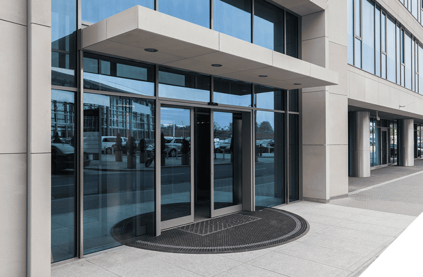 Modern glass entrance doors on an office building highlighting expert exterior door installation against a vibrant cityscape backdrop with passing cars.