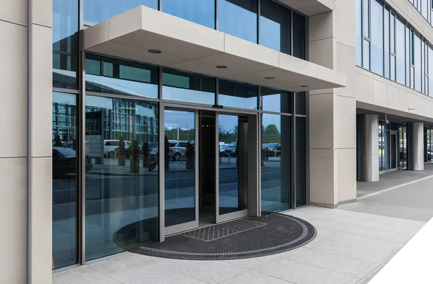 Modern glass entrance doors on an office building highlighting expert exterior door installation against a vibrant cityscape backdrop with passing cars.