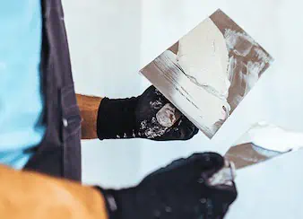 Close-up of skilled worker in black gloves applying white plaster with a trowel, showcasing expert remodeling and renovation techniques.