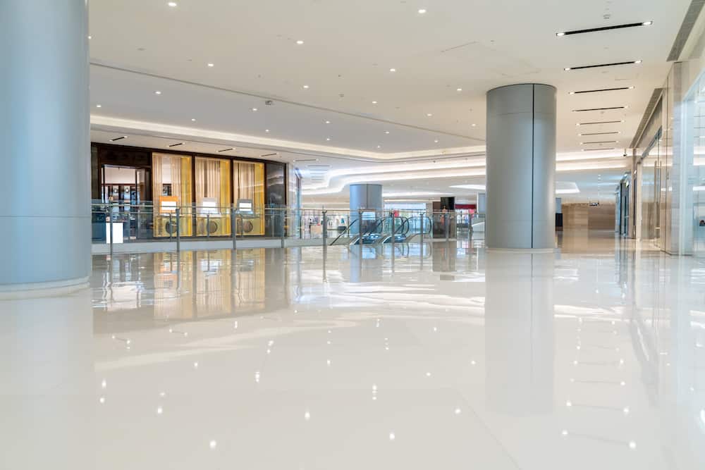 Modern shopping mall interiors with commercial flooring, bright ceiling lights, large pillars, and escalators creating an inviting ambiance.