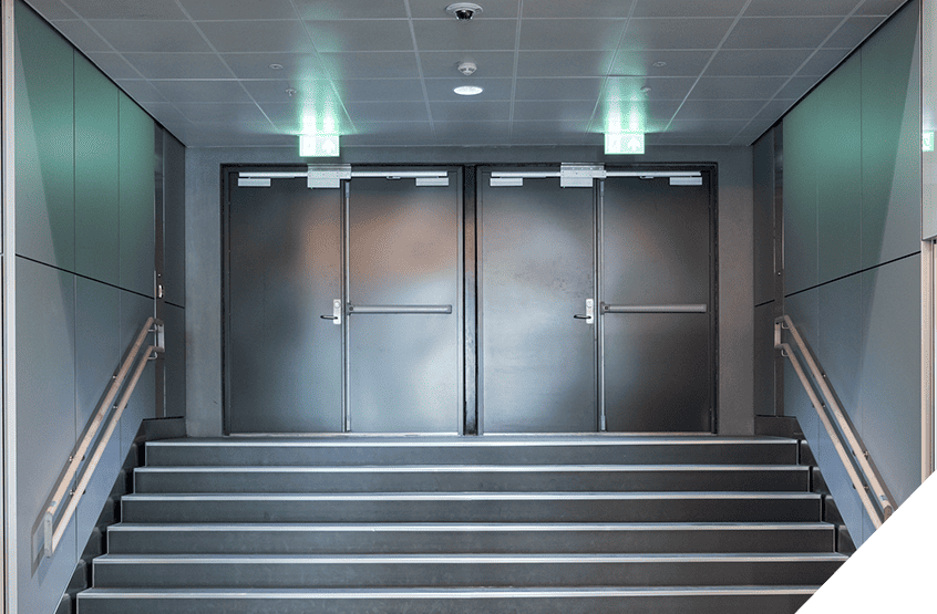 Modern stairway with dual metal exit doors, accentuated by sleek green wall panels and handrails in a contemporary hallway. Recent interior door installations enhance the space's aesthetic appeal, reflecting advanced construction techniques.