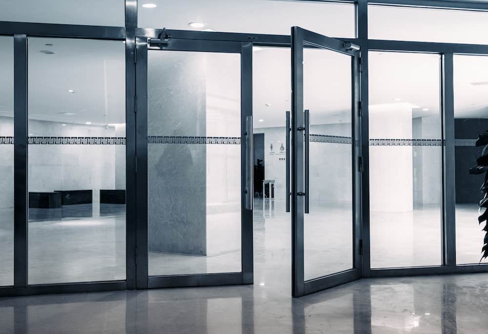 Open glass doors leading to a spacious, well-lit lobby with sleek marble floors and walls, highlighting expert interior door installation for renovation and construction services.
