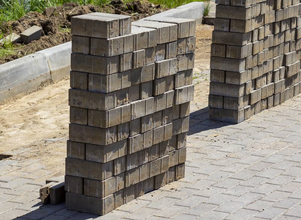 Partially built wall of stacked gray bricks on paved surface, illustrating expert masonry services with natural dirt and grass backdrop.