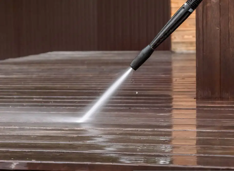 A person power washing a wooden deck, high-pressure water spray cleaning exterior surface.