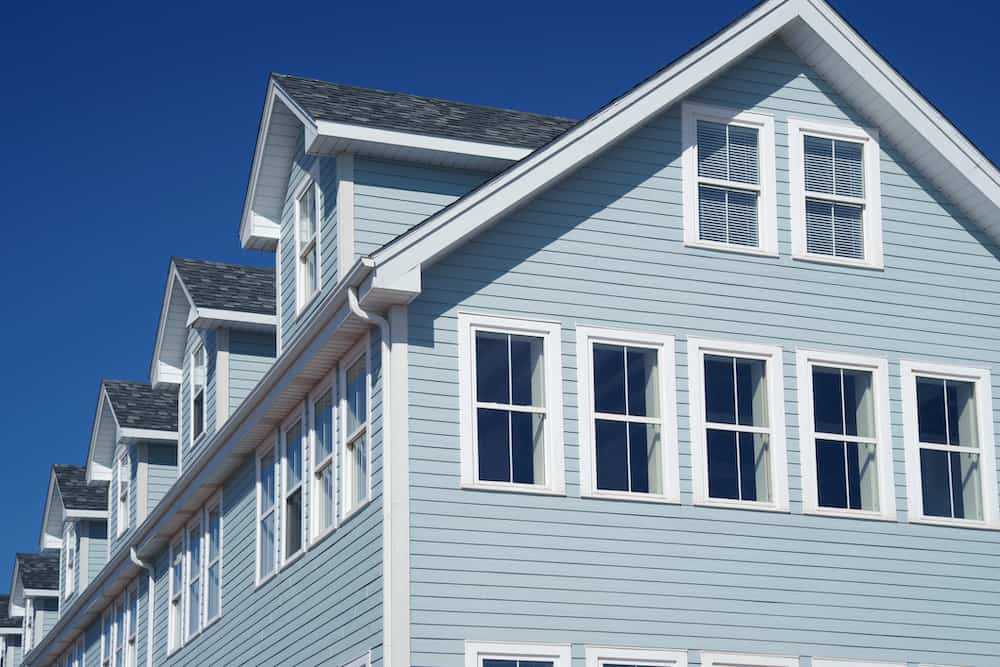 Modern light blue townhouses with white trim and multiple windows, highlighted against a clear blue sky, demonstrating expert siding renovation services.