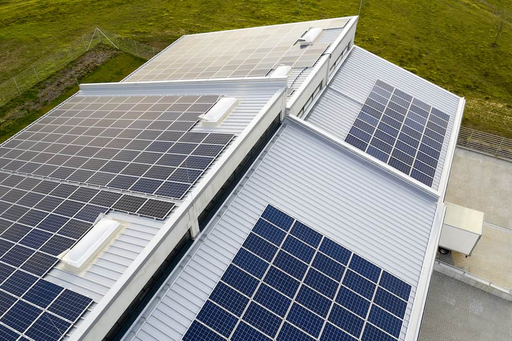 Aerial view of a building rooftop with solar panels, demonstrating efficient solar energy solutions on a sunny day, surrounded by lush green grass.