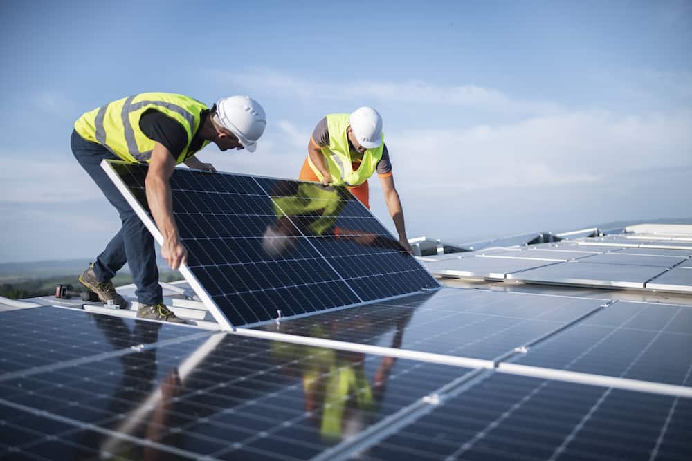 Workers in safety gear install solar panels on a rooftop, demonstrating expert renewable energy solutions under clear skies.