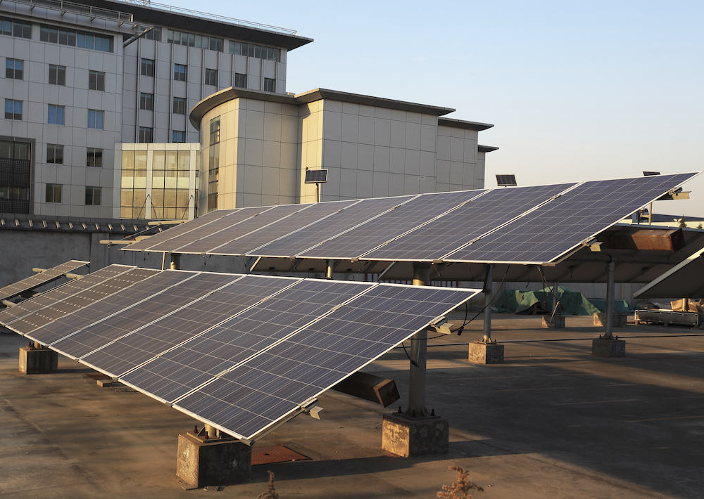 Solar panels installation on rooftop; modern building backdrop under clear sky; advanced solar services for energy efficiency improvement.