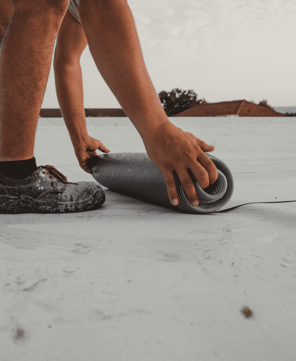 A skilled professional applies roofing material on a flat rooftop, demonstrating expert roofing services in durable work shoes.