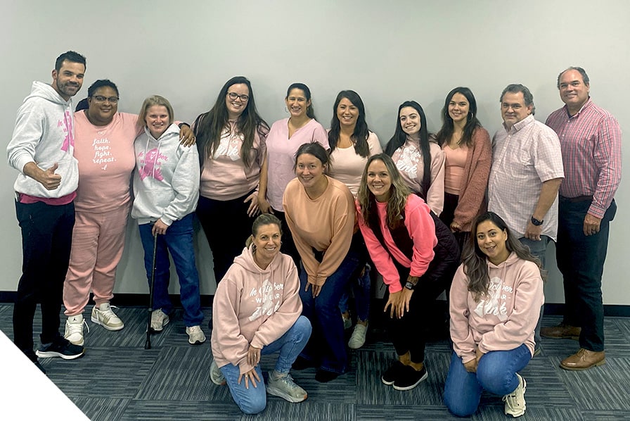 Fourteen people in vibrant pink attire smiling warmly, representing joy and unity; skilled renovation team offering comprehensive exterior and interior services.