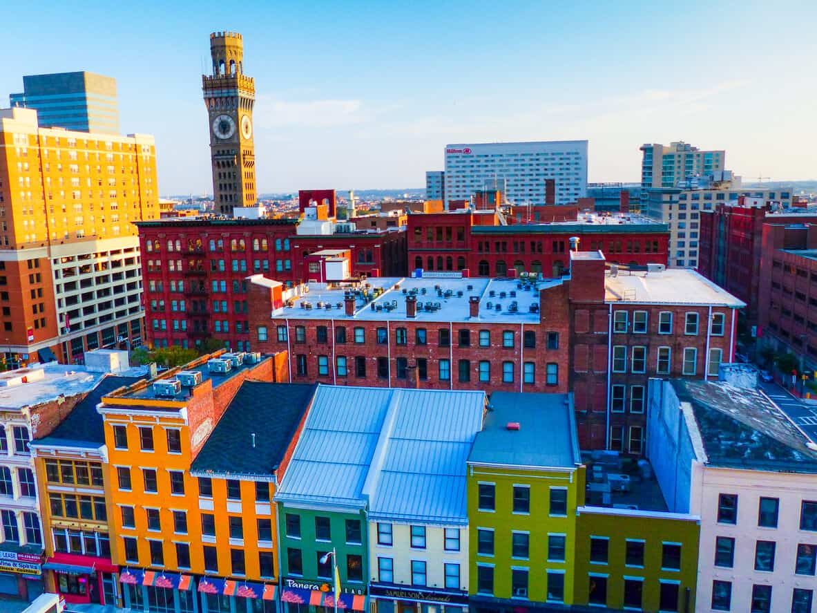 Vibrant cityscape featuring colorful renovated buildings, with a prominent clock tower and sleek modern structures under a clear blue sky.