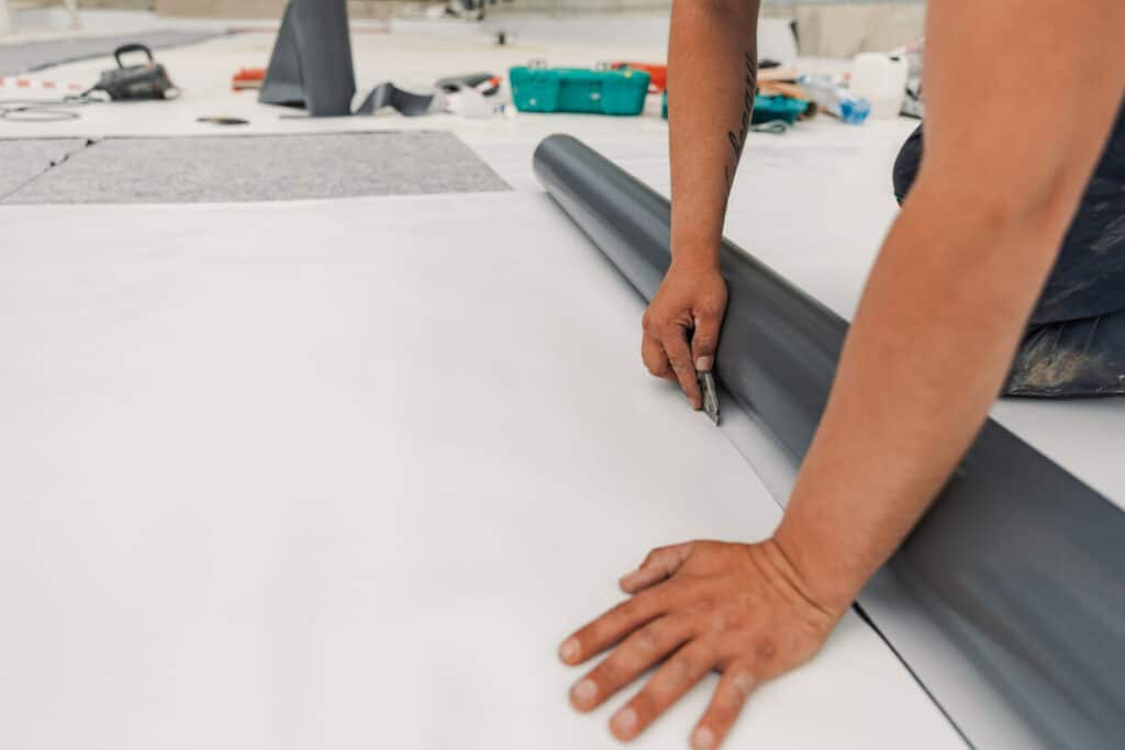Close-up of a worker cutting flooring material with a knife on a white sheet, surrounded by various construction tools and renovation supplies, highlighting precision and craftsmanship in renovation work.