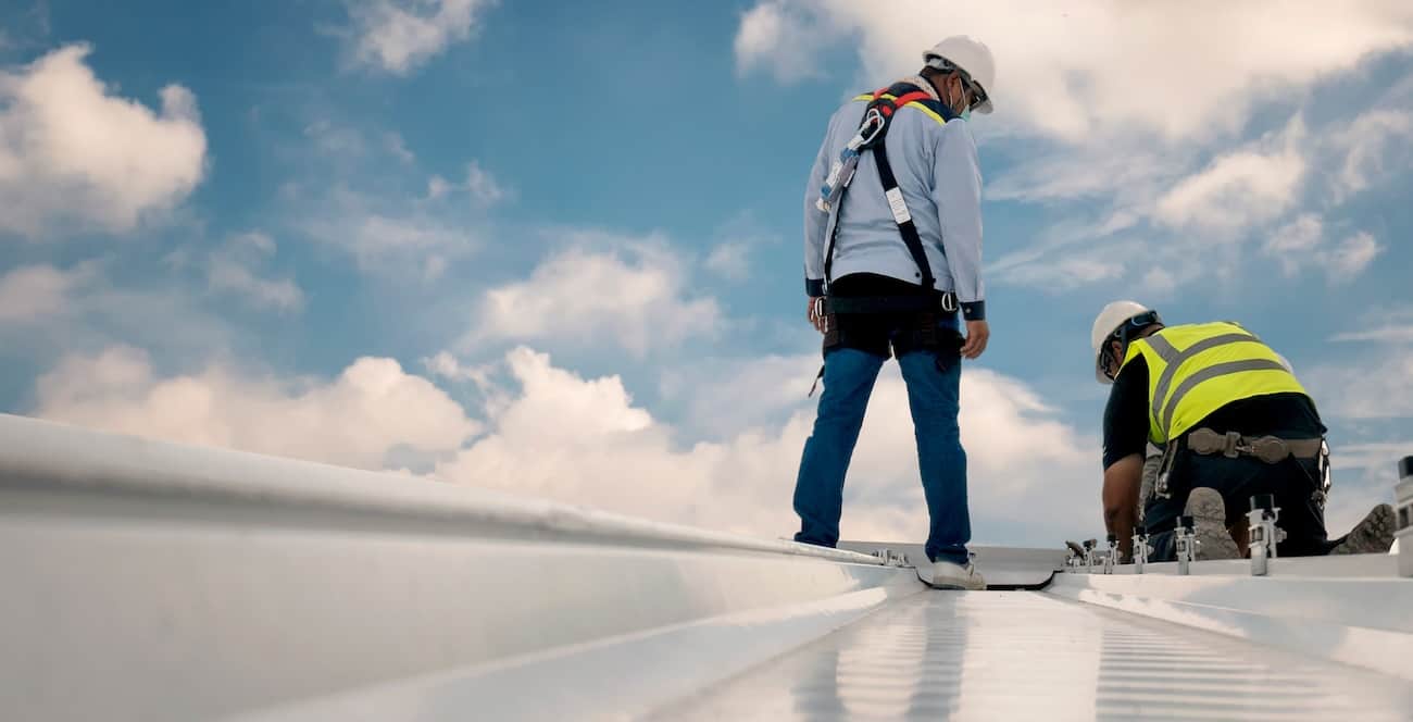 Two construction workers in safety gear performing commercial roof renovation under partly cloudy skies in Baltimore.