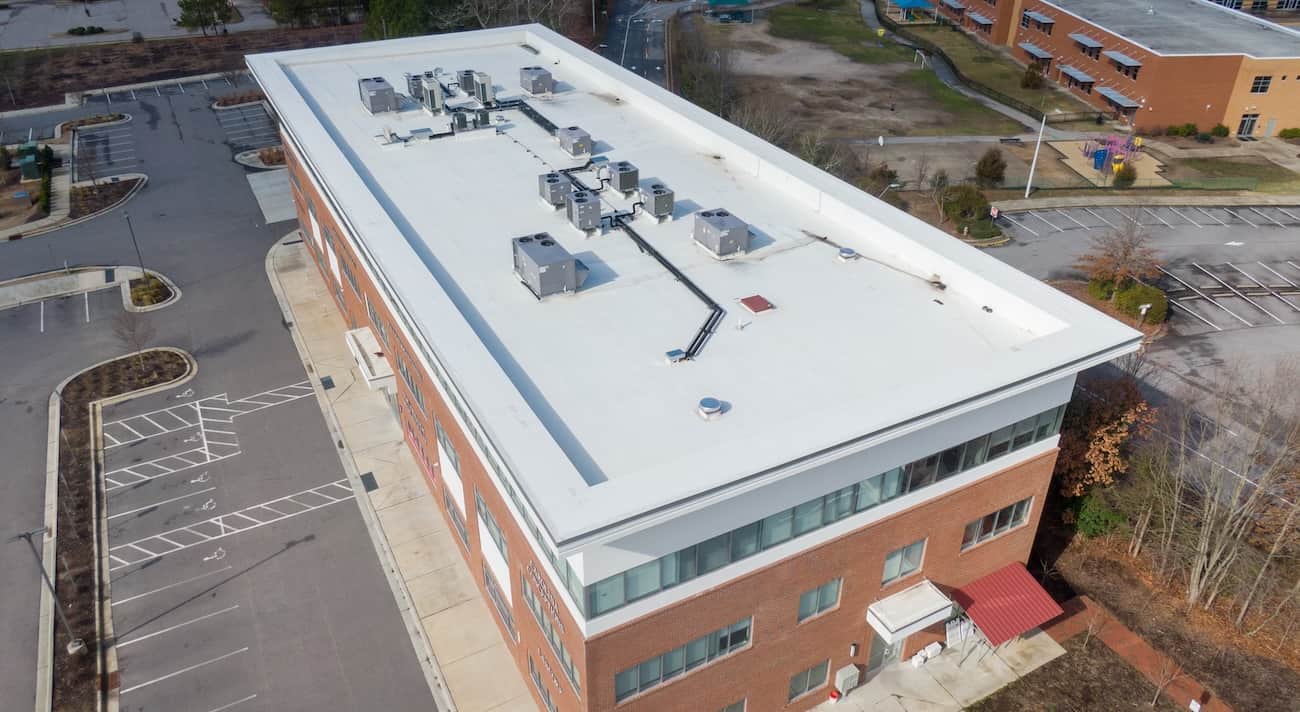 Aerial view of a commercial three-story brick building with flat roof, HVAC units visible, and an adjacent empty parking lot in Baltimore, highlighting exterior renovation and commercial roofing services.