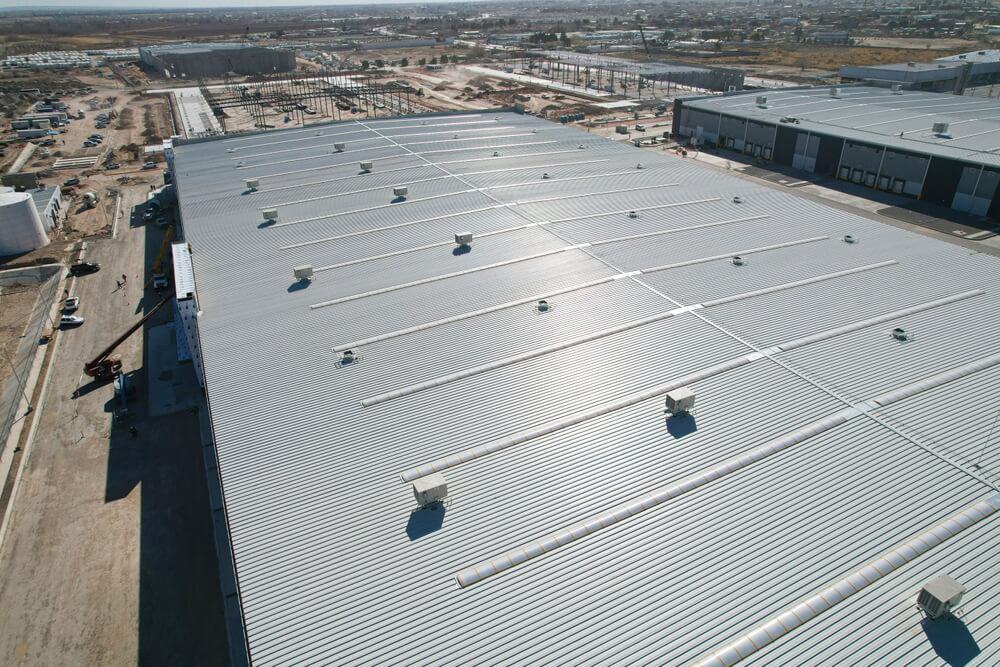 Aerial view of industrial warehouse showcasing commercial roofing, surrounded by construction and partially developed land in Fairfax, VA.