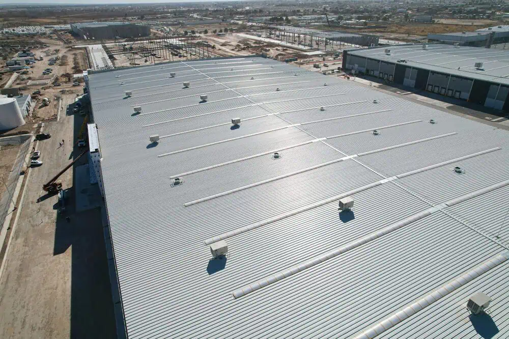 Aerial view of industrial warehouse showcasing commercial roofing, surrounded by construction and partially developed land in Fairfax, VA.