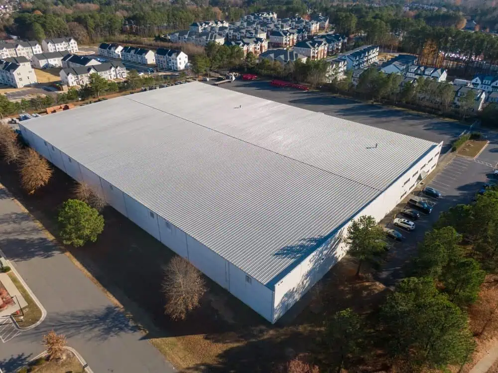 Metal roof on a large commercial warehouse surrounded by trees and homes