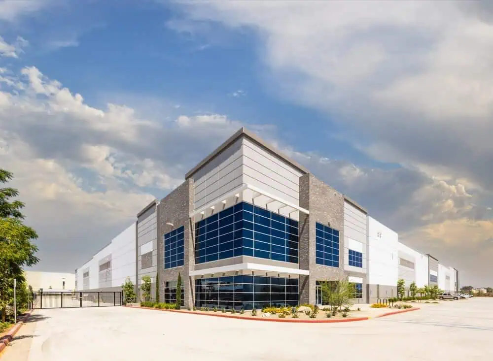 Large modern warehouse with stylish commercial siding and blue-tinted windows, set against a landscaped exterior under a partly cloudy sky. Ideal example of exterior renovation services.